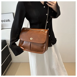 Detail of vintage brown shoulder bag with golden chain strap and buckle on model