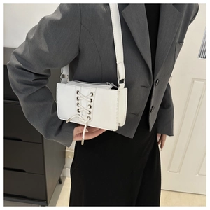 Détail du sac à bandoulière en cuir verni blanc avec lacets style corset et œillets métalliques