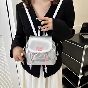 Detalle de mini mochila plateada metalizada con cordón rosa y etiqueta de logo de moda