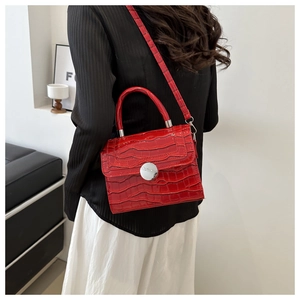 Detail of red croc-embossed handbag featuring a silver round buckle and slim shoulder strap