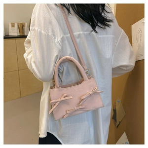 Détail du sac bandoulière rose avec nœuds porté par un mannequin dans un cadre épuré