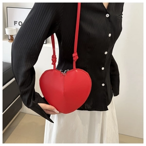 Detail of red heart-shaped crossbody bag with silver zippers and knots on thin straps