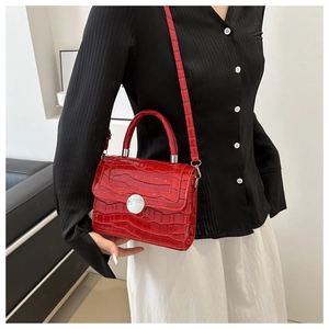 Detail of red crocodile texture handbag with large silver round buckle and shoulder strap