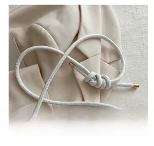 Detail of white handbag strap with elegant knot and gold metallic tips on beige blazer