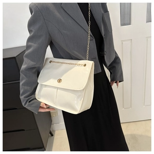 Close-up of white patent leather shoulder bag with gold chain and turn-lock closure
