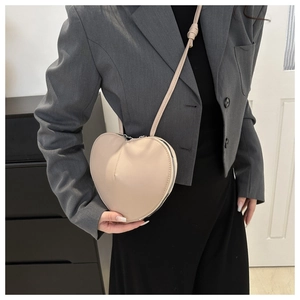 Detailed view of beige heart-shaped leather crossbody bag styled with a gray blazer