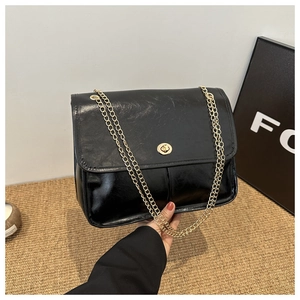 Detail of black faux wax leather handbag with golden chain strap and round twist lock clasp