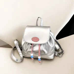 Detalle de mini mochila plateada con cordones rosas y cuentas azules en una silla beige