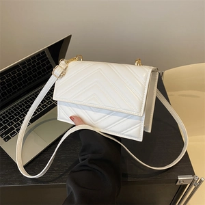 Sac bandoulière blanc avec matelassage en V et détails dorés sur un bureau