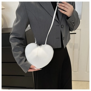 Model wearing white heart-shaped crossbody bag with dual metal zippers and slim strap