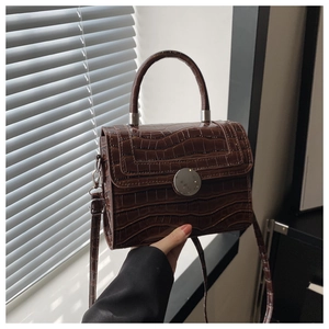 Detail of dark brown crocodile pattern handbag featuring a round silver metallic clasp