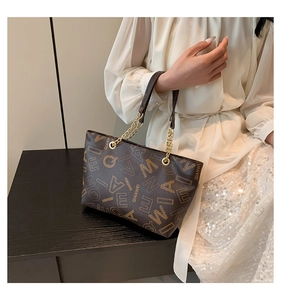 Detailed close-up of a brown leather tote bag featuring gold chain and logo pattern