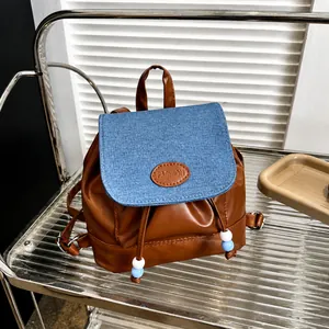 Detalle de mini mochila con solapa de mezclilla, cuentas y cordón de cuero marrón