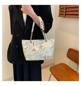 Detail of white tote bag featuring black letter print and golden chain strap detail