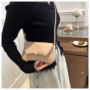 Detail of a minimalist beige crossbody bag featuring a square golden metal buckle and smooth leather