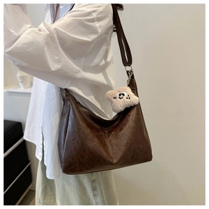 Dettaglio della borsa tote in pelle marrone scuro con un ciondolo smiley in peluche