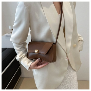 Close-up of brown leather crossbody bag with gold rectangular buckle on white blazer