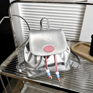 Detalle de mini mochila plateada metalizada con cordón rosa y parche con logotipo