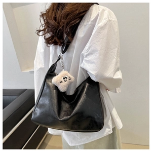 Dettaglio della borsa hobo in pelle nera con ciondolo morbido sulla spalla della modella