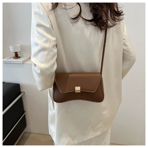 Detail of stylish dark brown leather shoulder bag with gold clasp on white blazer outfit