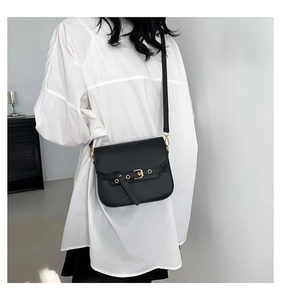 Detail of classic black saddle bag with golden buckle and textured vintage leather finish