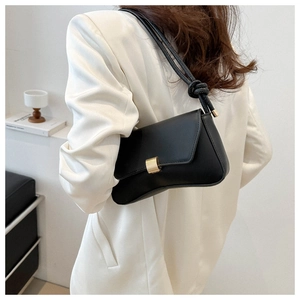 Close-up of minimalist black leather shoulder bag with golden metal buckle and knotted strap