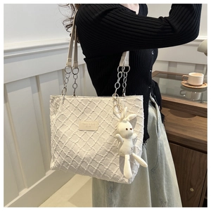 Close-up of white quilted tote bag texture with rabbit charm and leather chain strap