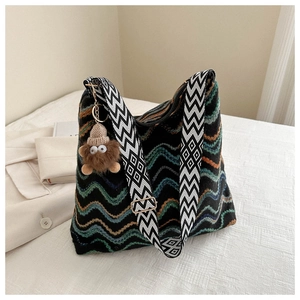 Close-up of knit bucket bag with wave patterns, wide geometric strap and plush charm