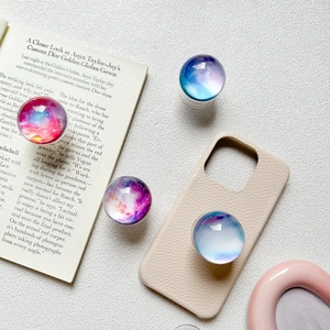 Round collapsible nebula star phone grip on a beige leather case with aesthetic props