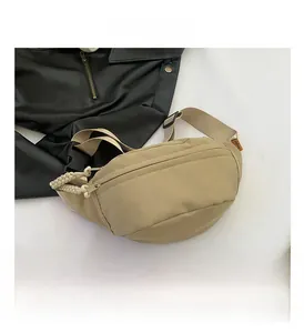 Detail of beige nylon crossbody bag featuring a woven zipper pull and orange side label