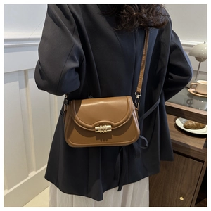 Modèle portant un sac selle en cuir marron caramel avec fermoir doré détaillé
