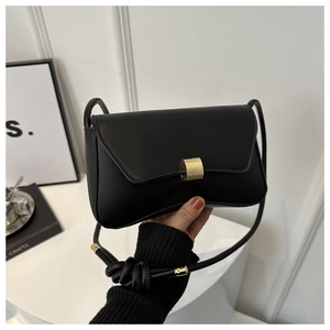 Detail of minimalist black leather shoulder bag with gold metal buckle and knotted strap