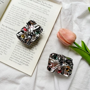Detail of metallic pleated phone grip with colorful gemstones on a white fabric background