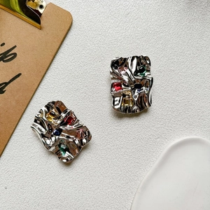 Close-up of metallic crumpled earrings featuring colorful multi-gemstone rectangular inlay