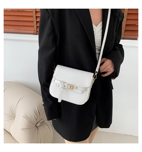 Close-up of a white leather saddle bag with buckle detail worn with a black blazer