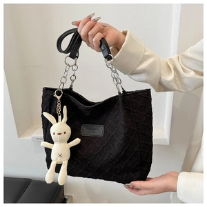 Close-up of black quilted tote bag with silver chain strap and white rabbit charm accessory