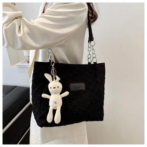 Black quilted tote bag with rabbit pendant and chain strap worn by a female model