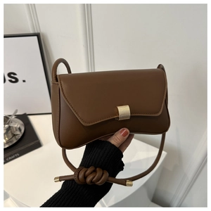 Close-up of brown baguette bag featuring gold metal buckle and knotted leather strap details