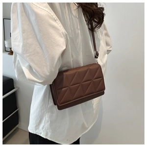 Detail of brown quilted square crossbody bag with adjustable leather strap worn by a model