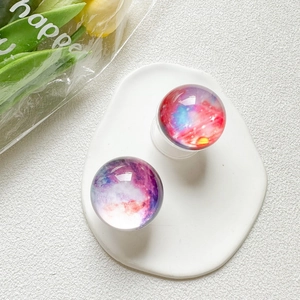 Close-up of two crystal galaxy nebula phone grips displayed on a white ceramic plate