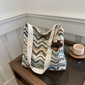 Retro zigzag woven bucket bag with wide strap and plush pendant on wooden surface