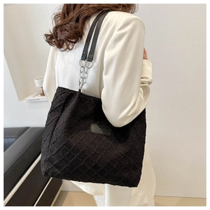 Detail of black textured tote bag featuring a chain shoulder strap and square pattern