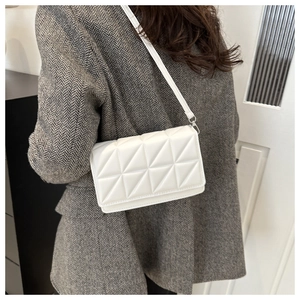 Detailed view of white quilted crossbody bag with geometric triangle stitching on a model