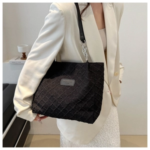 Detail of black quilted tote bag with chain strap and fashion label on textured fabric