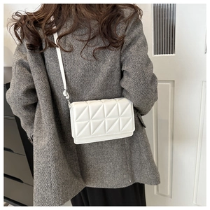 Detailed view of white quilted crossbody bag with geometric triangular pattern over gray coat