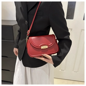 Modèle portant un sac sous le bras en cuir rouge avec boucle dorée sur un blazer noir chic