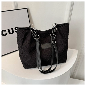 Detail of black quilted tote bag with silver chain handle and textured fabric finish