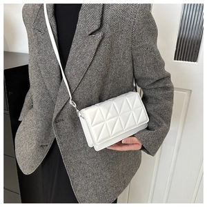 Close-up of white quilted crossbody bag with geometric pattern on grey suit