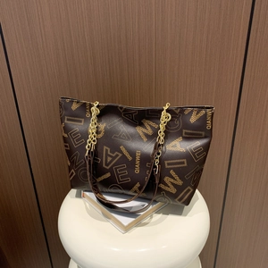 Elegant dark brown tote bag with letter print and gold chain strap on white stool
