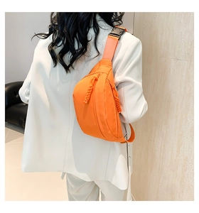Detail of vibrant orange nylon chest bag featuring woven rope zippers and durable plastic buckle